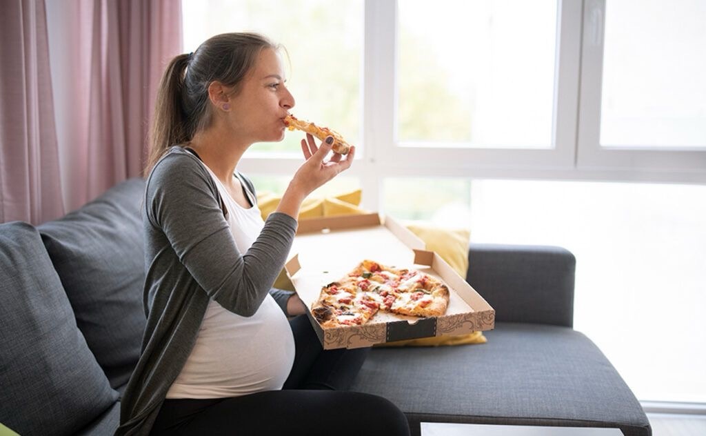 A pregnant lady eating pizza
